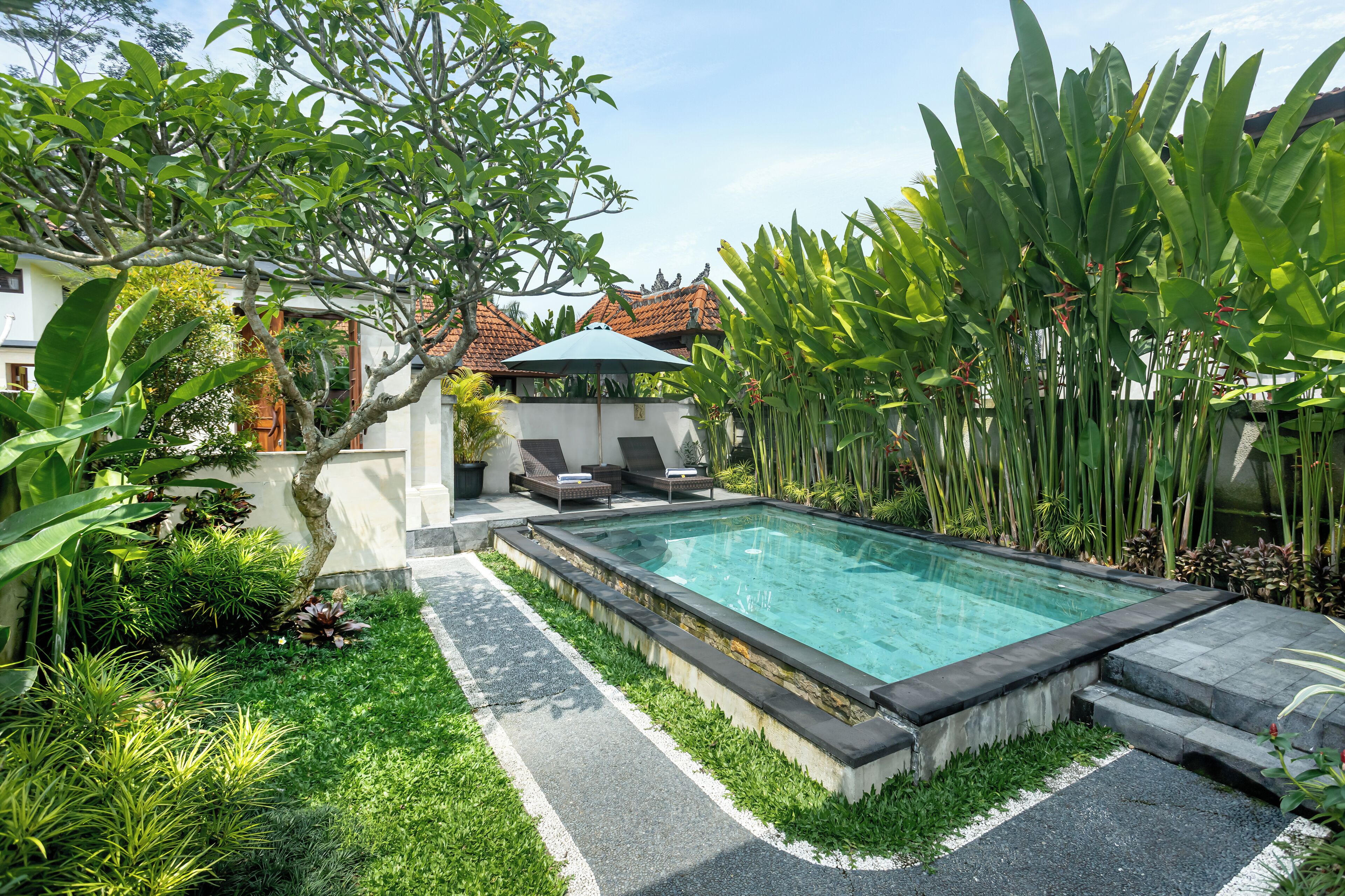 A swimming pool surrounded by lush greenery and a small patio area with a table and chairs.