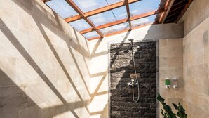 A modern bathroom with a stone shower wall, a skylight, and a tiled floor. - The Sakara Ubud Villas (Tegallalang)