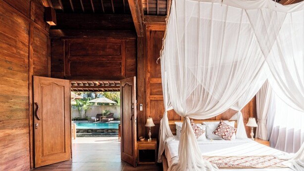 A wooden room with a bed under a canopy, a wooden door, and a view of an outdoor pool. - The Sakara Ubud Villas (Tegallalang)