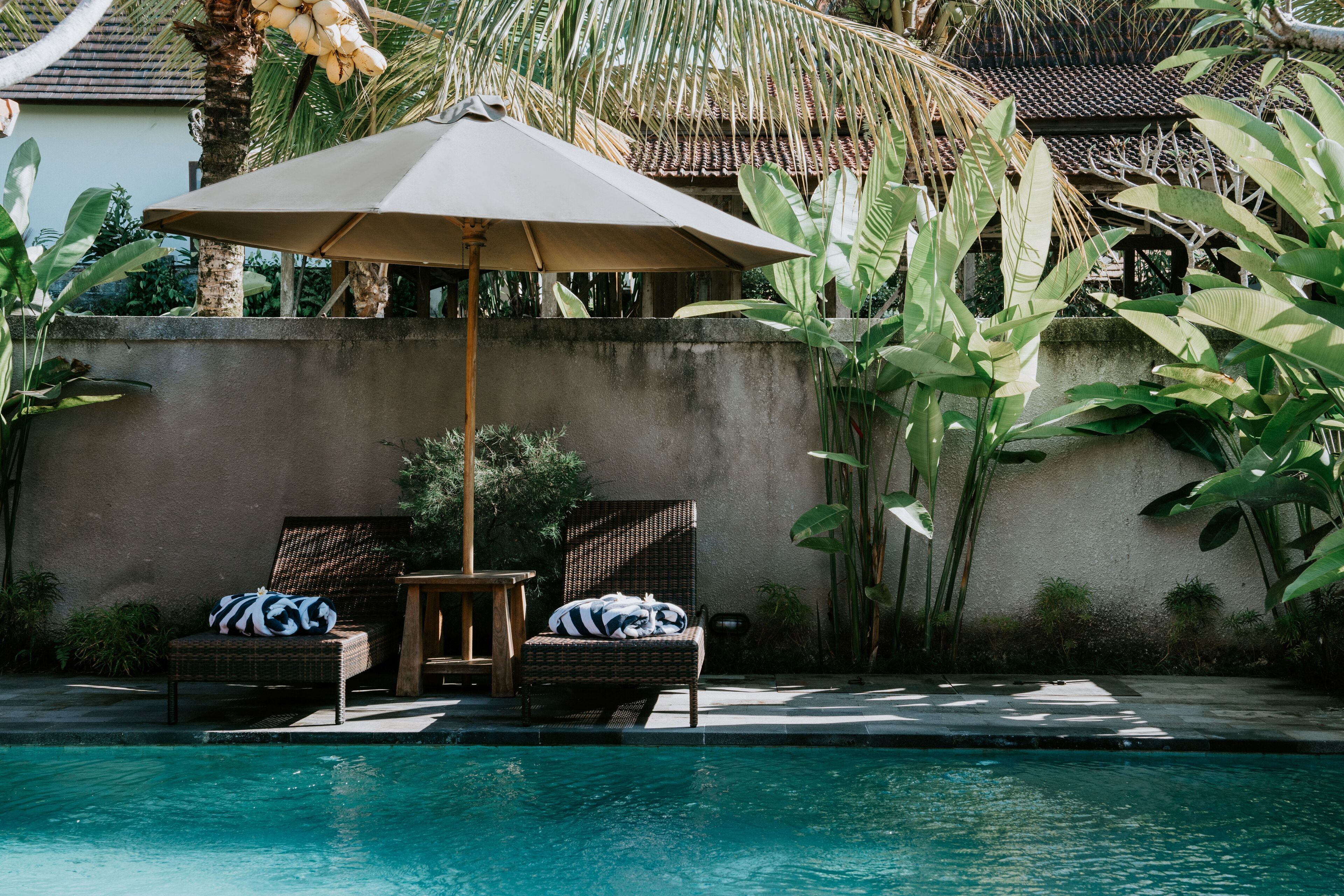 A poolside area with two wicker lounge chairs, a table, and an umbrella.
