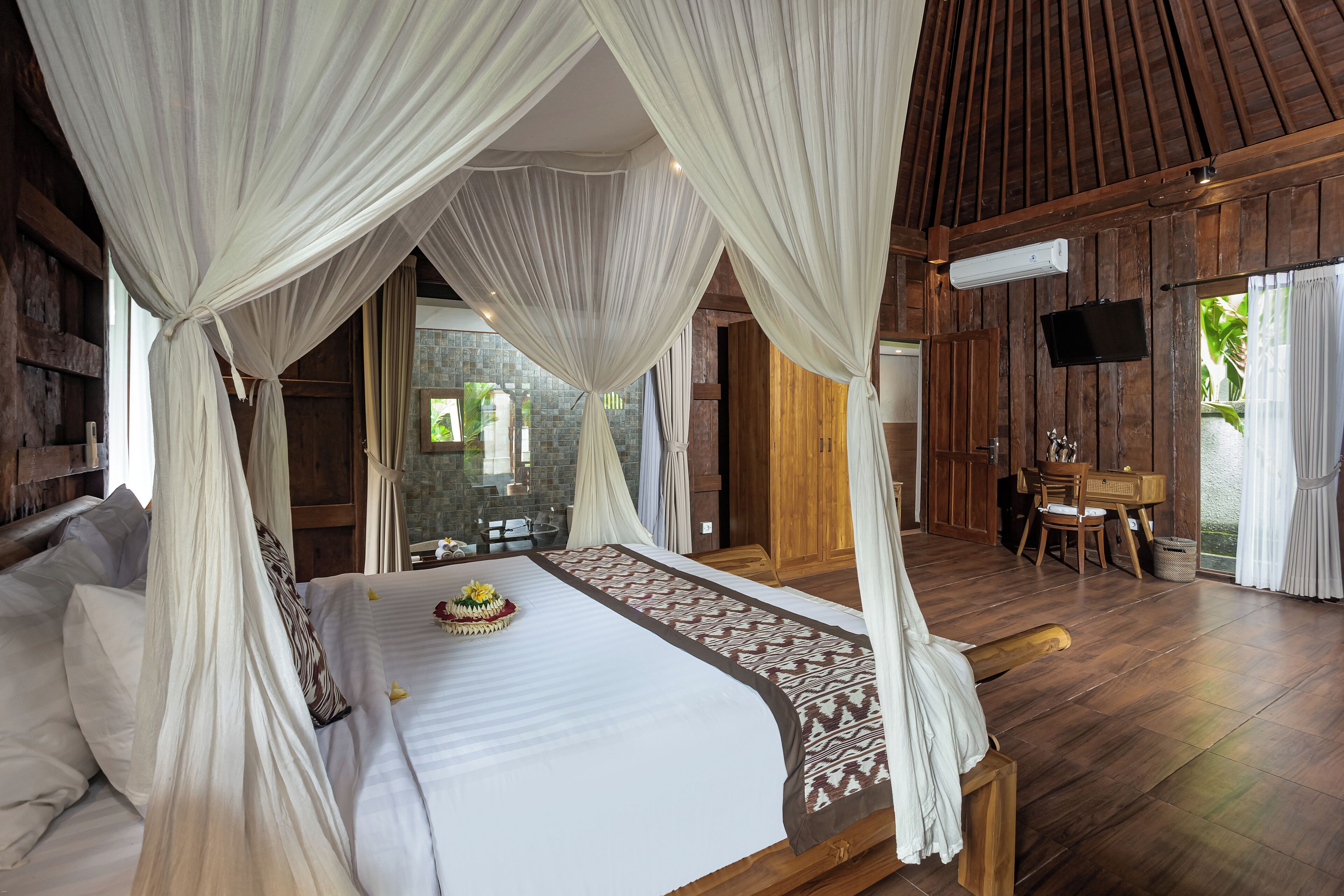 A bedroom with a canopy bed, wooden flooring, and a TV mounted on the wall.