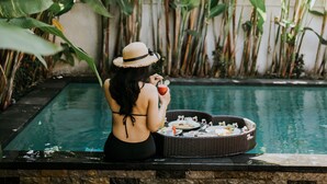 A woman sitting by a pool with a wicker basket containing food, surrounded by large green plants. - The Sakara Ubud Villas (Tegallalang)