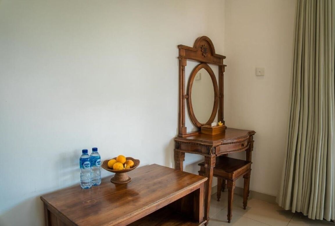 Un bureau en bois, un miroir, un saladier de fruits et deux bouteilles d’eau.