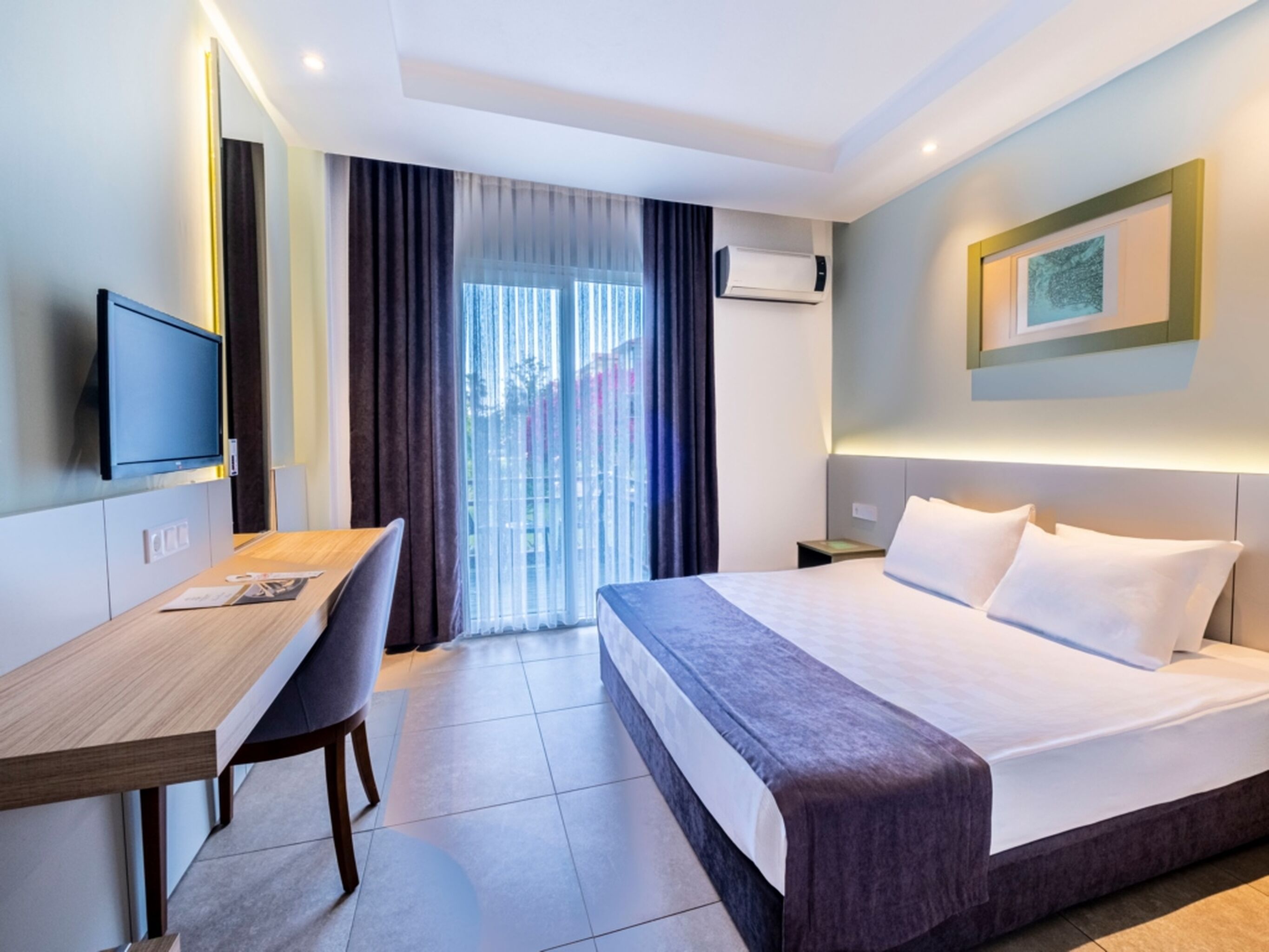 A hotel room with a bed, a desk, a chair, a television, and a window with curtains.
