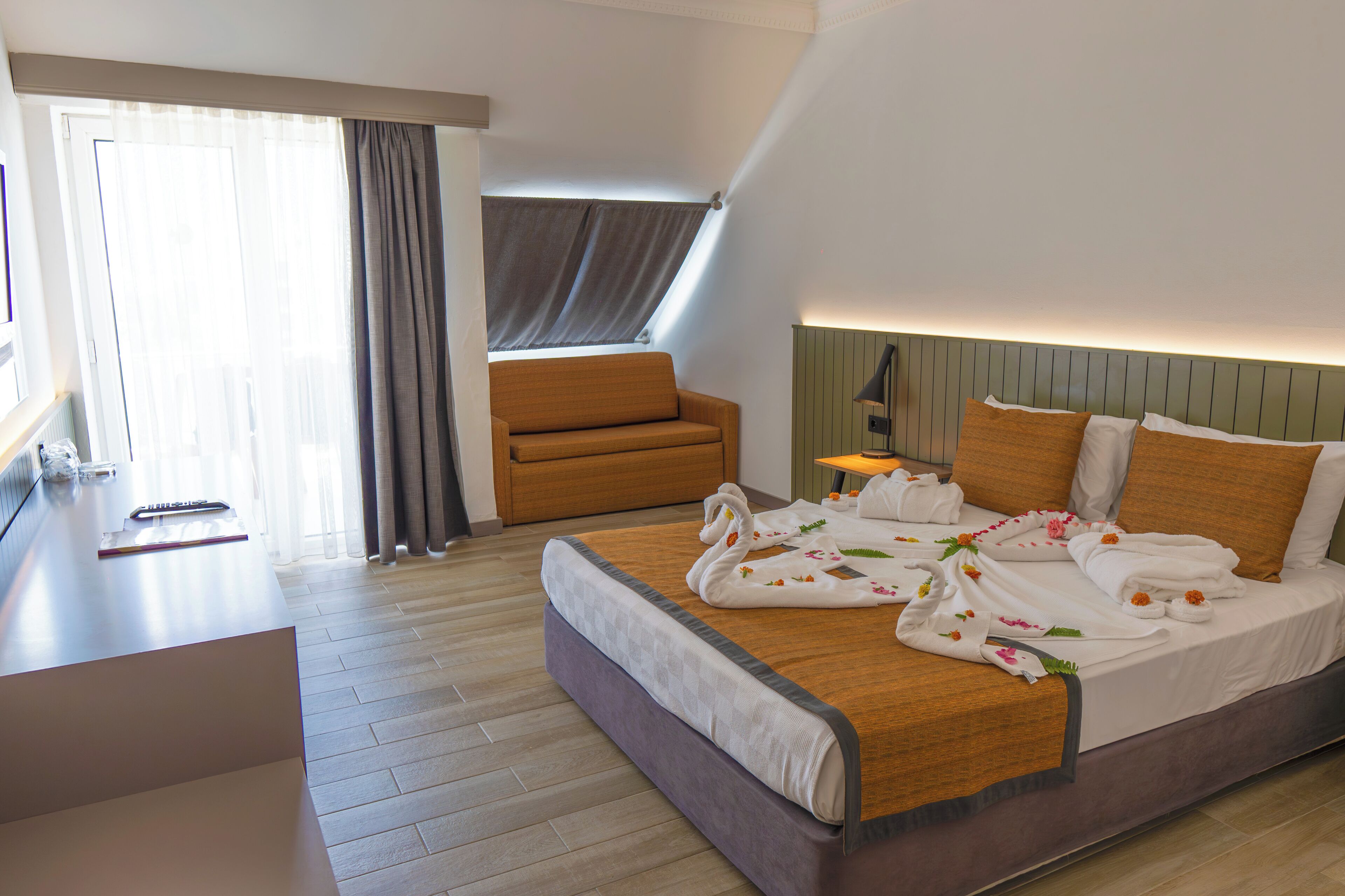 A hotel room with a bed, a sofa, a desk, and a window with curtains.