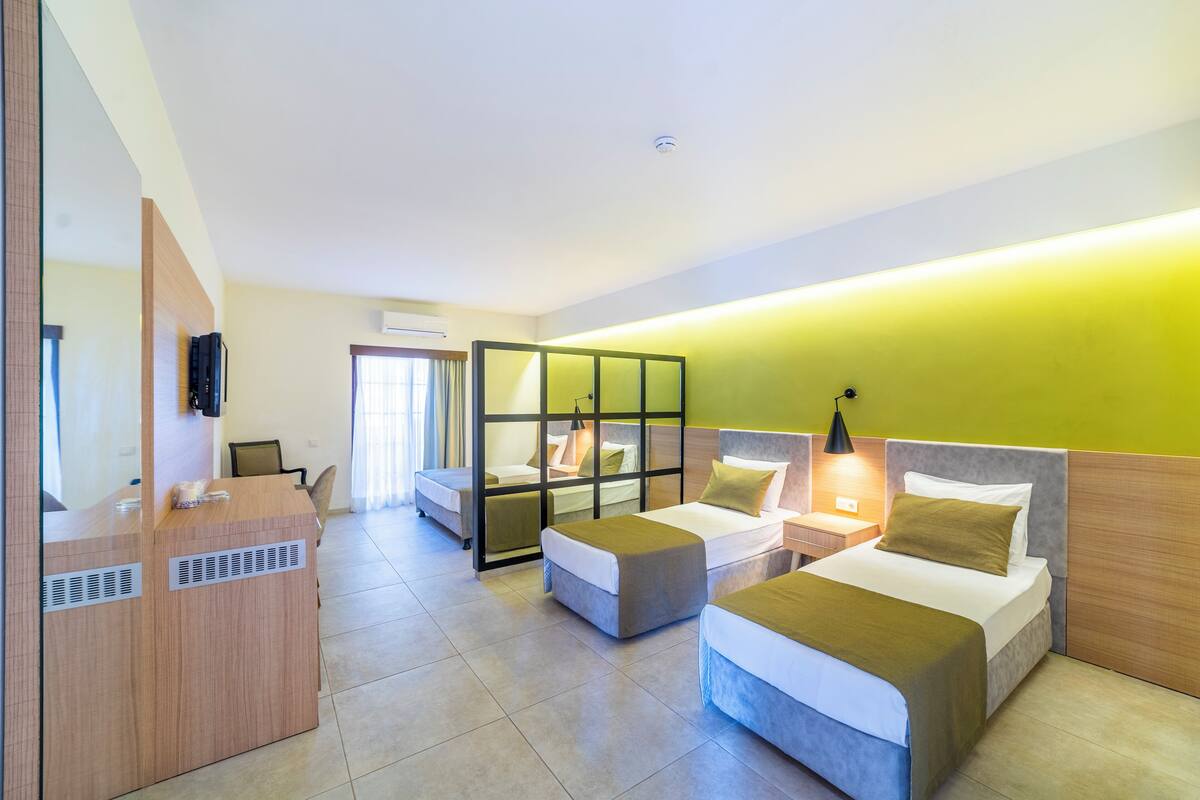 A hotel room with a reception desk, two beds with headboards, a desk lamp, and a window with curtains.