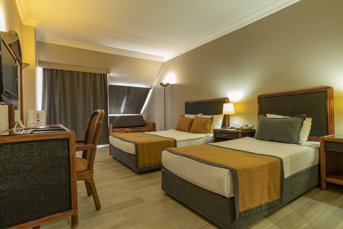 A hotel room with two beds, a desk, a chair, and a television.