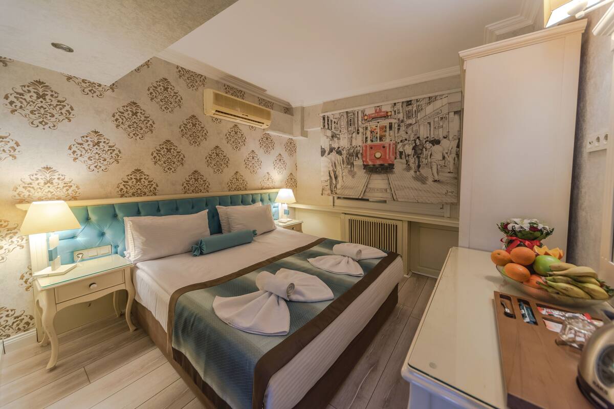 A hotel room with a large bed, a nightstand with a lamp, a wall-mounted air conditioner, and a fruit bowl on the dresser.