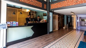 A reception area with a black counter, two staff members, a decorative wall, and a patterned rug. - Viva Deluxe Hotel (Istanbul)