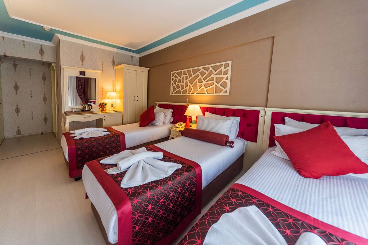A hotel room with three beds, a vanity with a mirror, and a wall-mounted artwork.