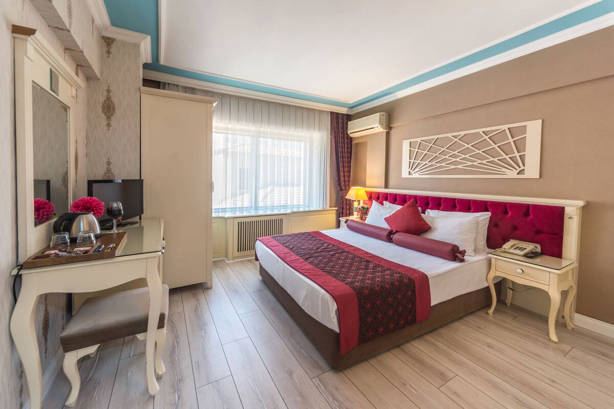 A hotel room with a bed, bedside table, desk, chair, and a window with curtains.
