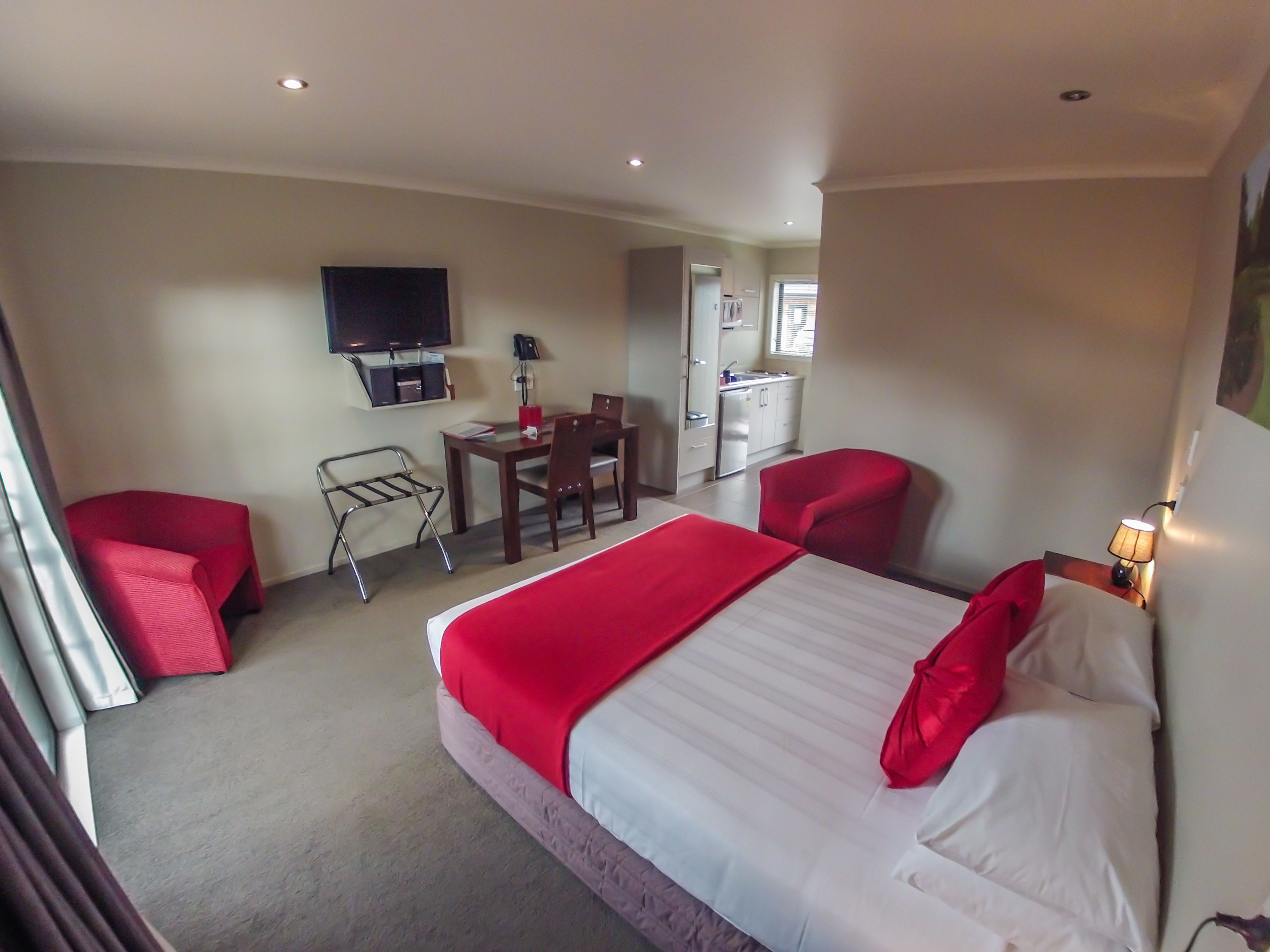 Una habitación de hotel con cama, escritorio, silla, televisor y kitchenette.