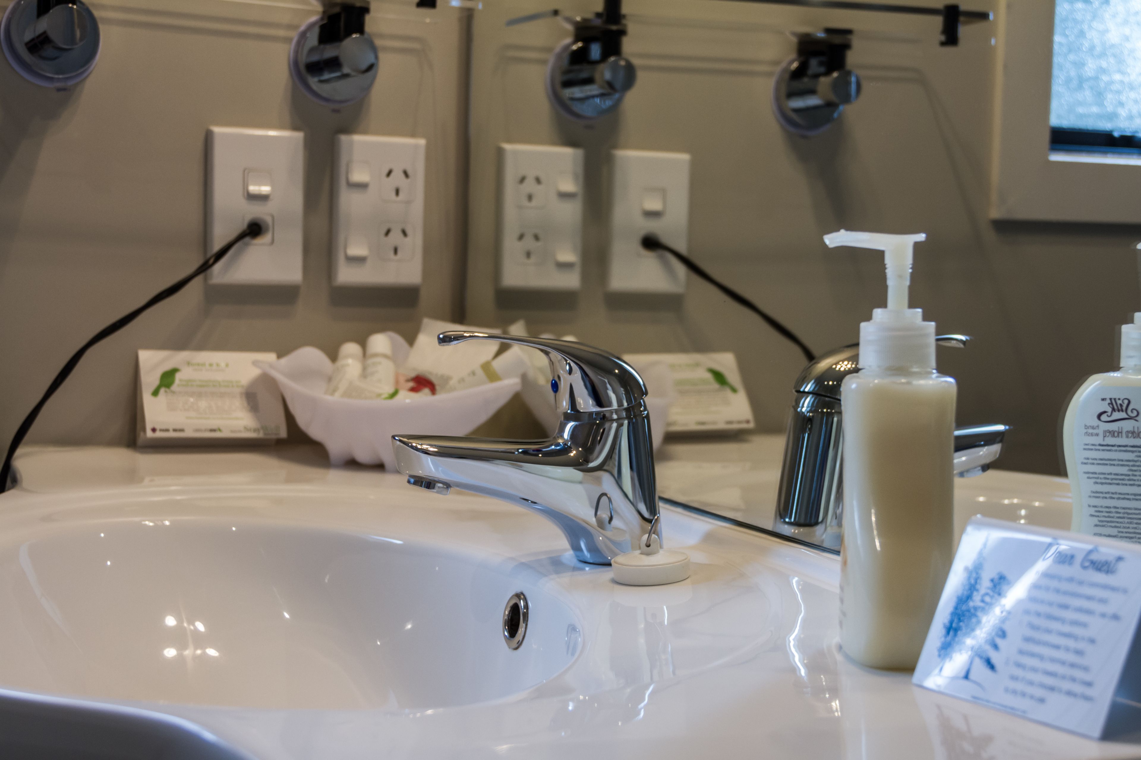A bathroom sink with a chrome faucet, a soap dispenser, and a bowl of toiletries.