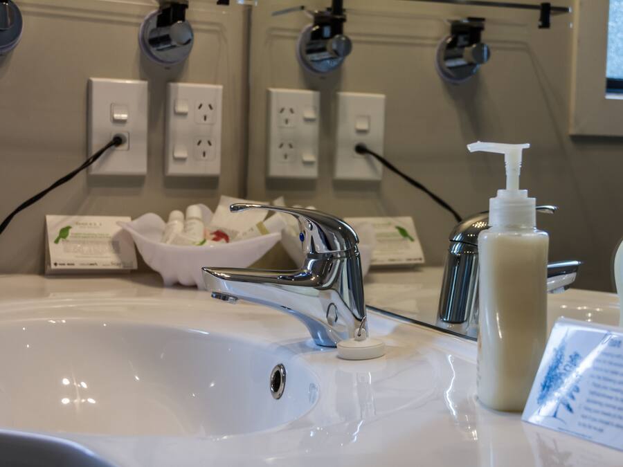 Un lavabo de salle de bain avec un robinet chromé, un distributeur de savon et un bol contenant des articles de toilette.