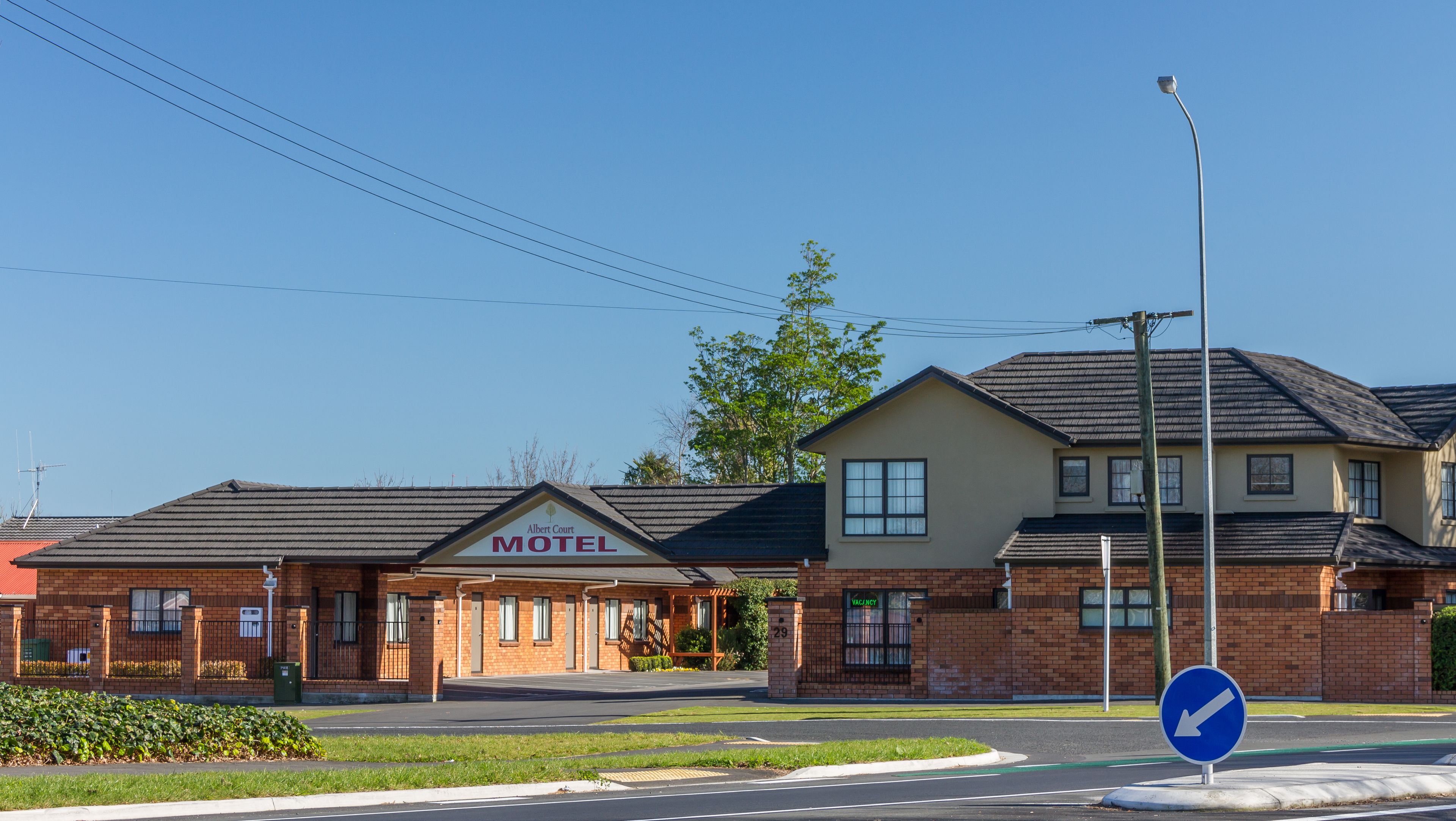 A motel with a brick facade, a sign reading "Albert Court Motel," and a blue directional sign on the street.