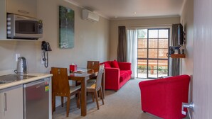 A compact living space with a kitchenette, dining area, and a red sofa. - Albert Court Motor Lodge (Hamilton)
