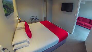 Een hotelkamer met een bed, een aan de muur bevestigde televisie, een rode bank in de aangrenzende zithoek, en een landschapsschilderij aan de wand.