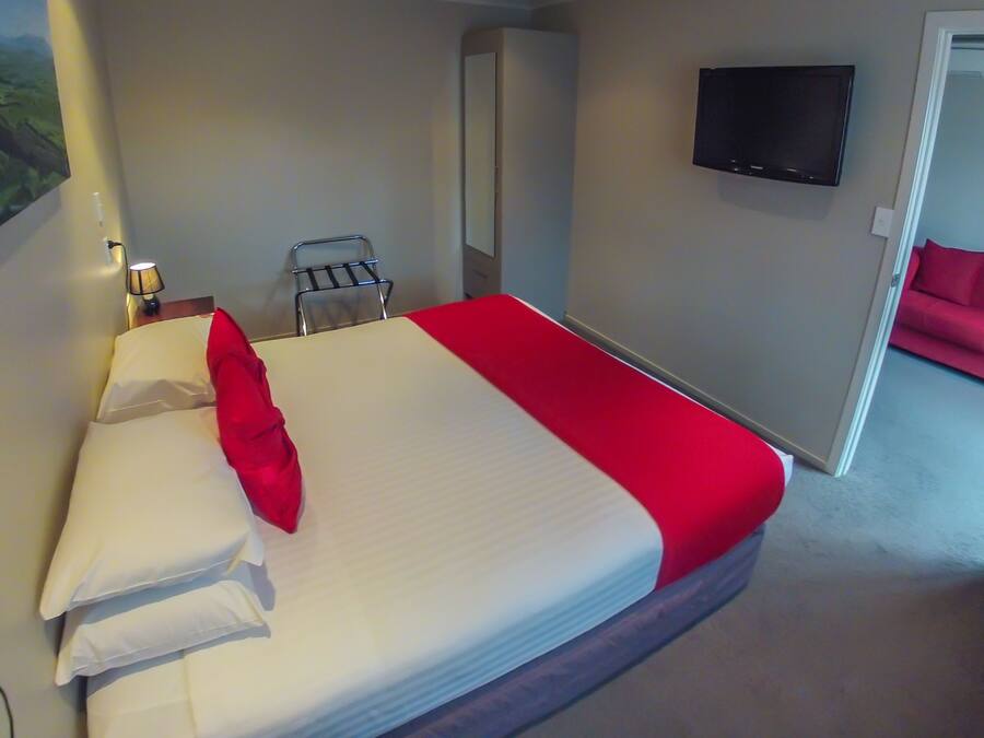 Een hotelkamer met een bed, een aan de muur bevestigde televisie, een rode bank in de aangrenzende zithoek, en een landschapsschilderij aan de wand.