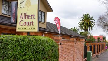 A motel named Albert Court with a signboard, a brick wall, and a well-maintained hedge.