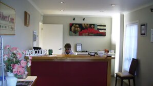 A reception desk with a 'welcome' sign, a framed picture on the wall, and a chair to the right. - Albert Court Motor Lodge (Hamilton)
