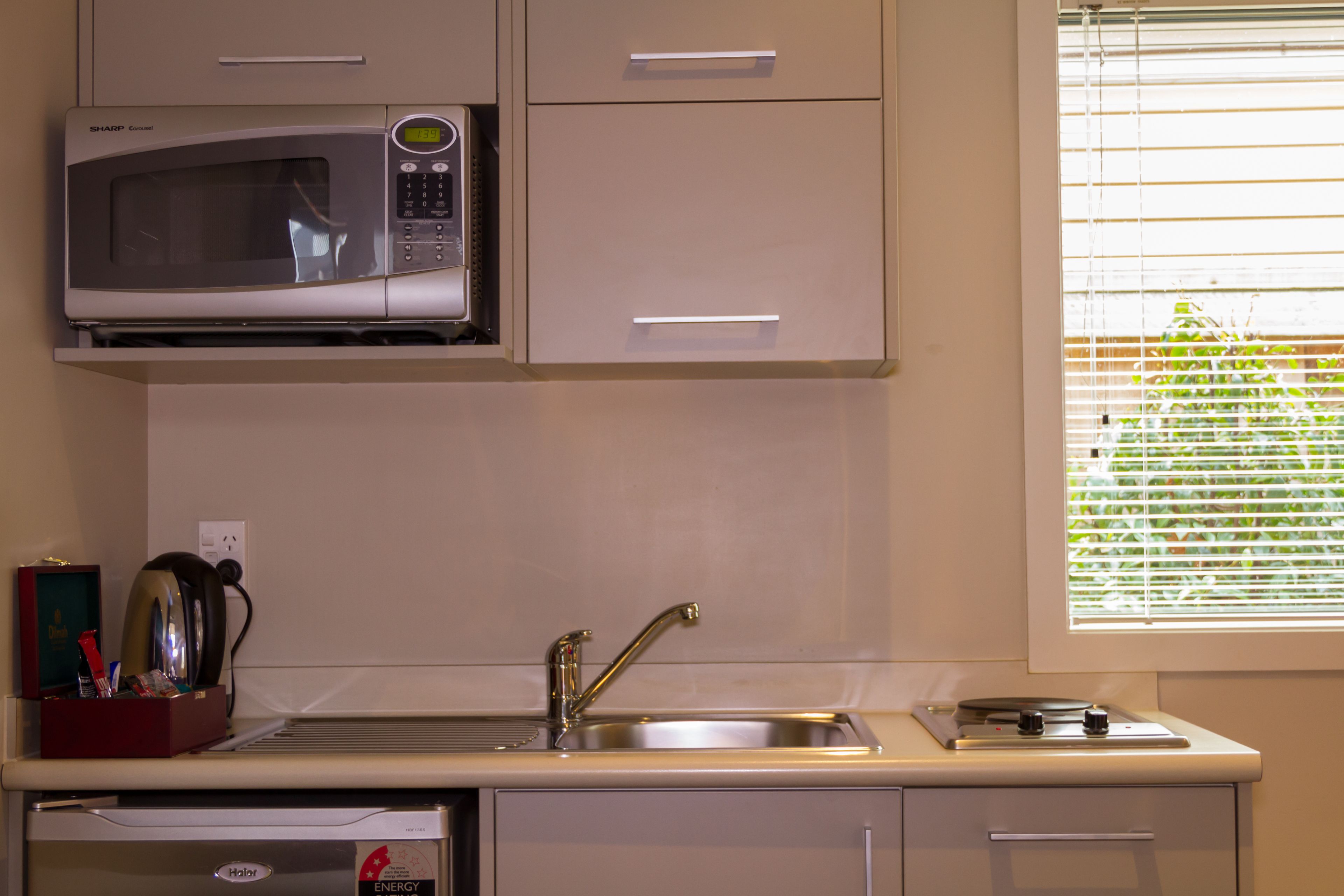 Une cuisine équipée d’un four à micro-ondes, d’un évier et d’une fenêtre avec des stores.