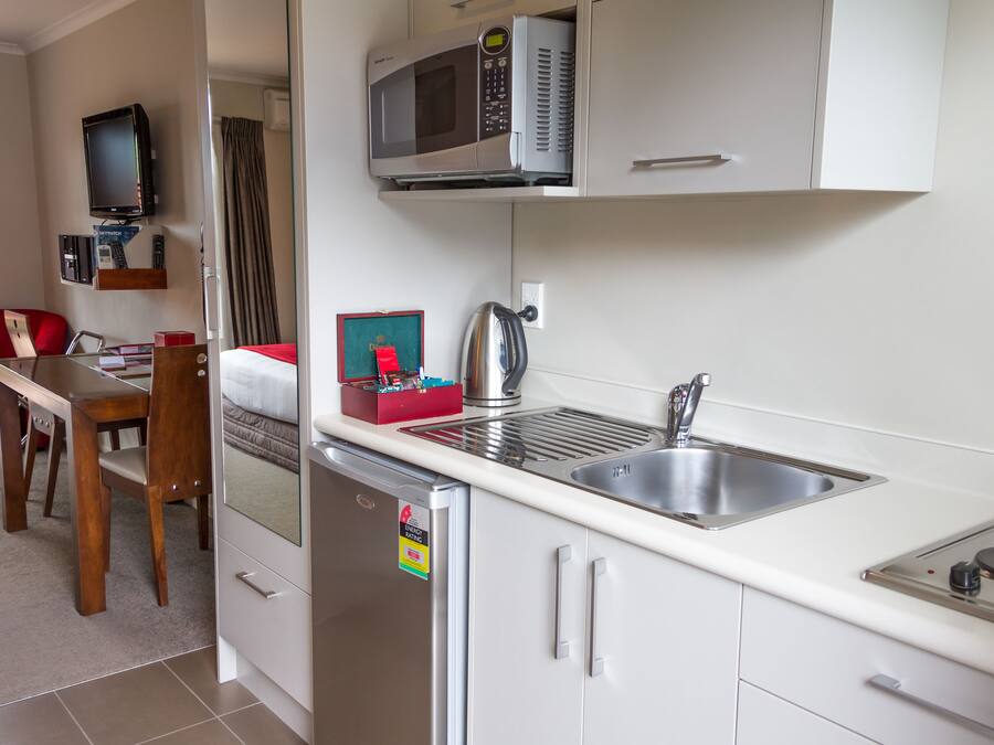 A compact kitchen with a microwave, a sink, and a small refrigerator. There is a wooden dining table and a red chair.