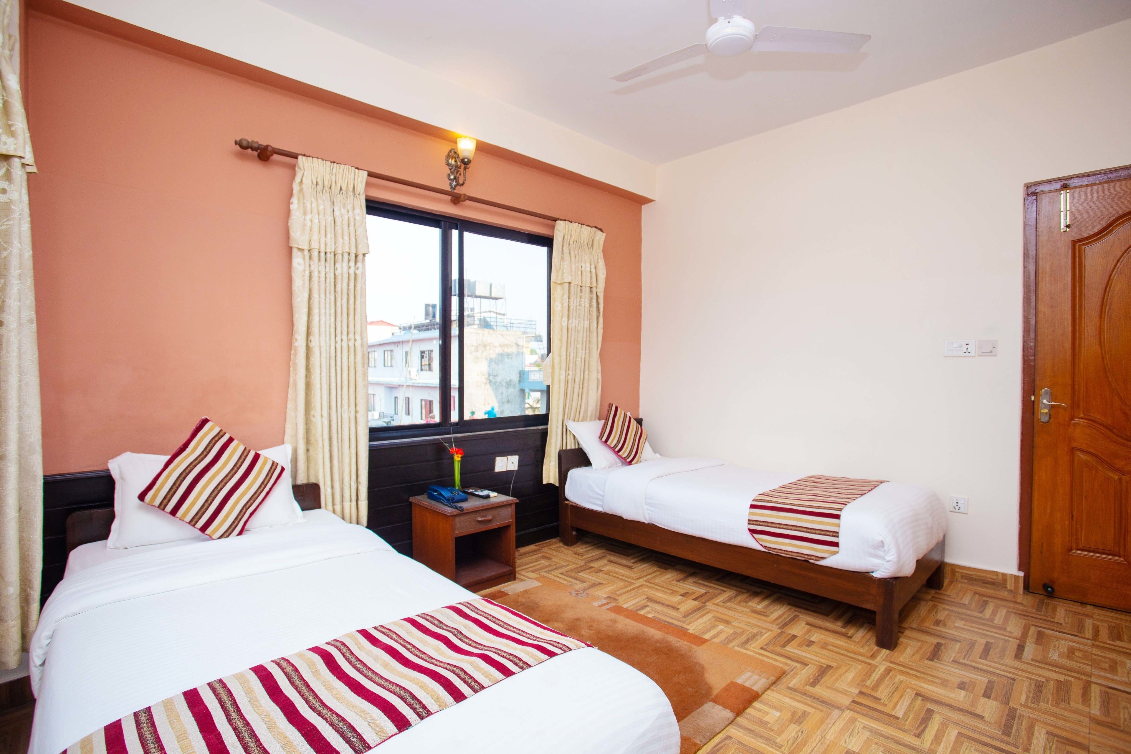 A hotel room with two beds, a window with curtains, a nightstand, and a wooden door.