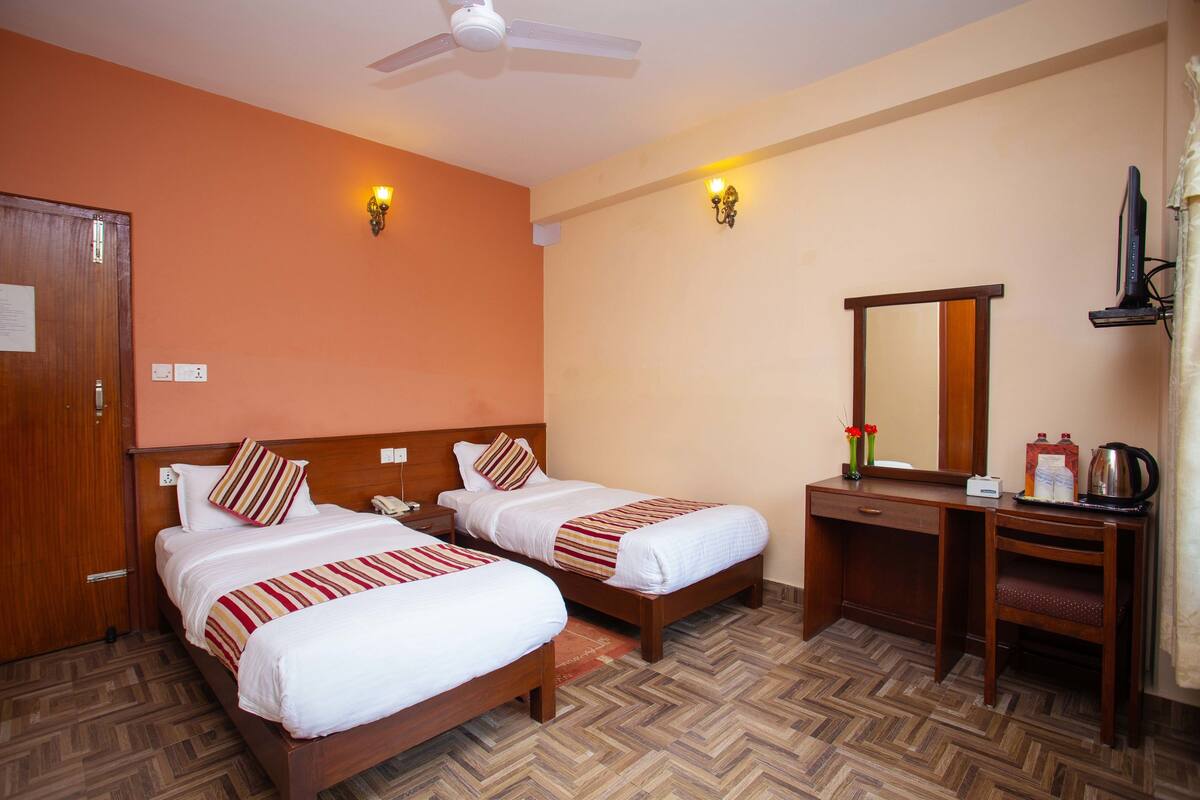A hotel room with two beds, a desk, a chair, a mirror, and a ceiling fan.