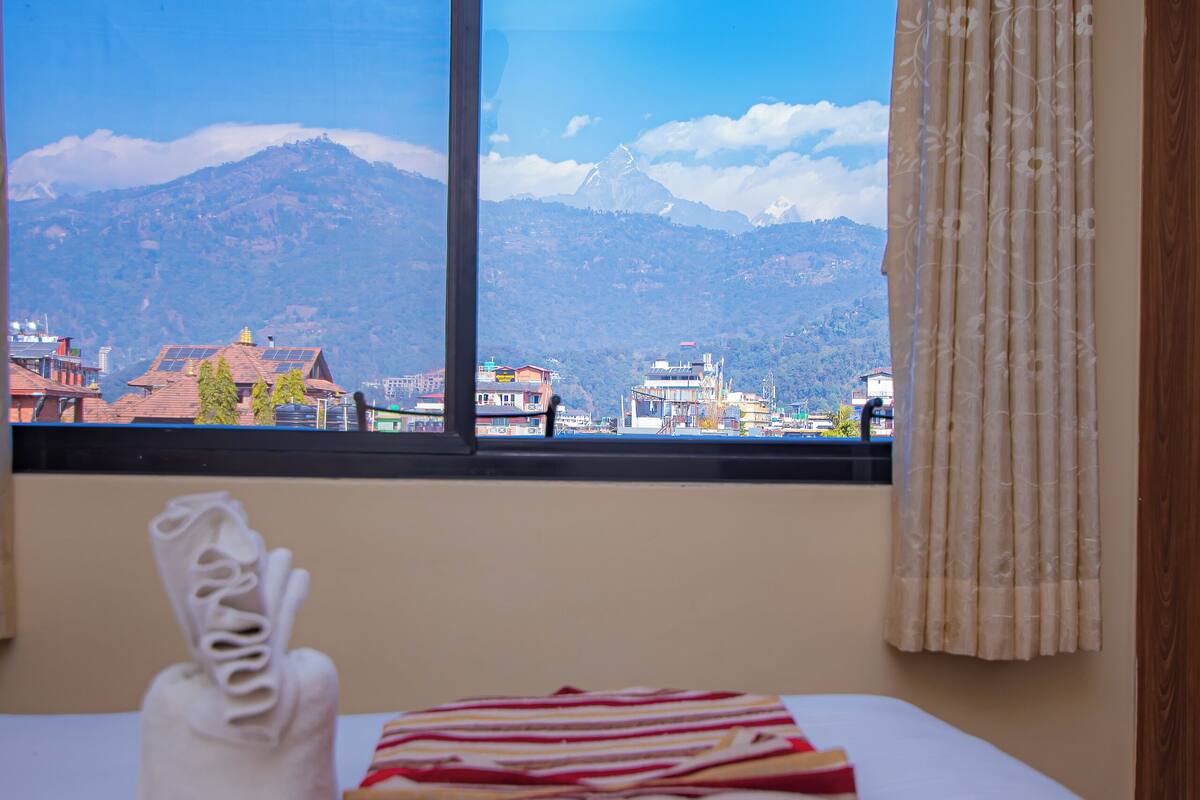 A hotel room with a bed, a window with a view of mountains, and a curtain.