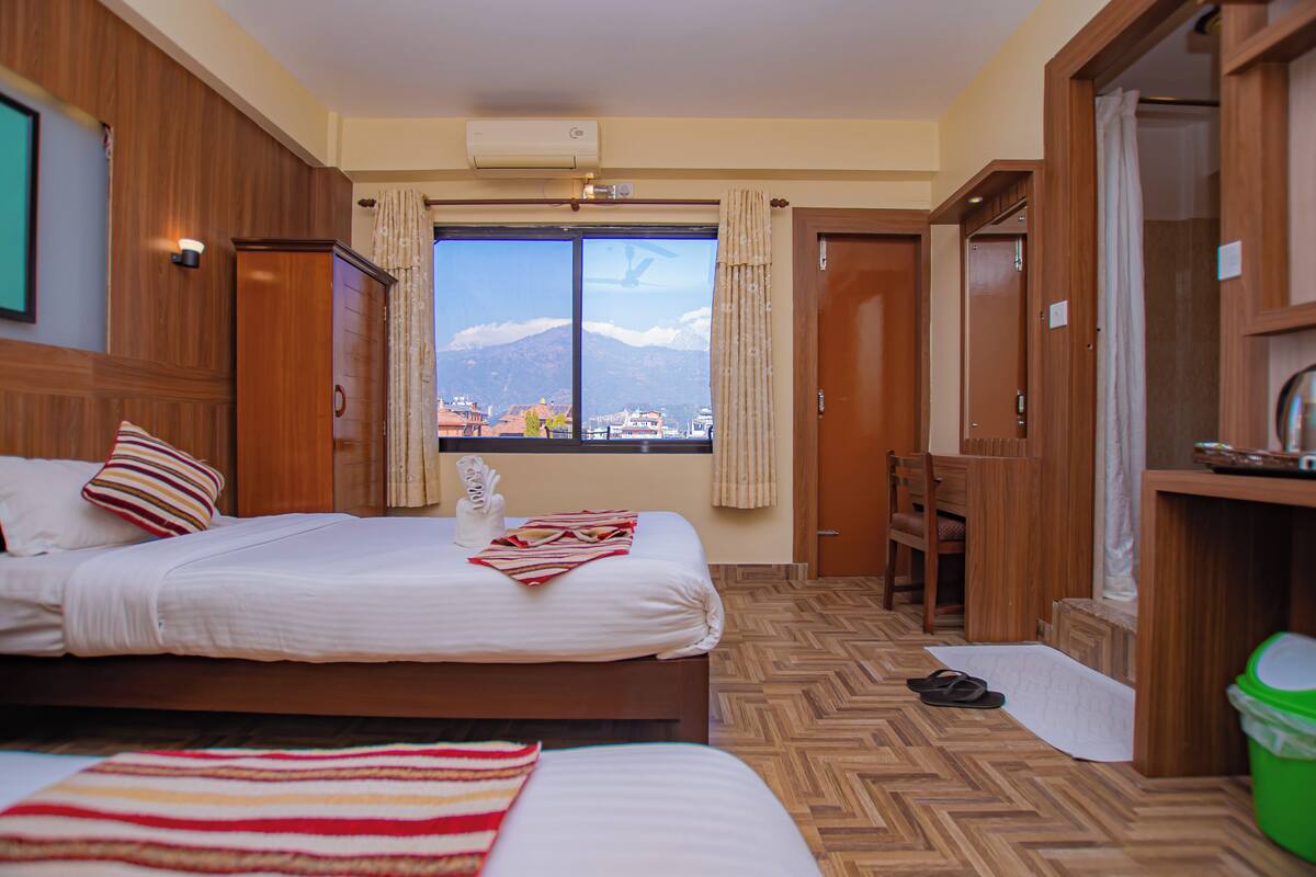 A hotel room with a bed, a chair, a desk, and a view of a mountain.