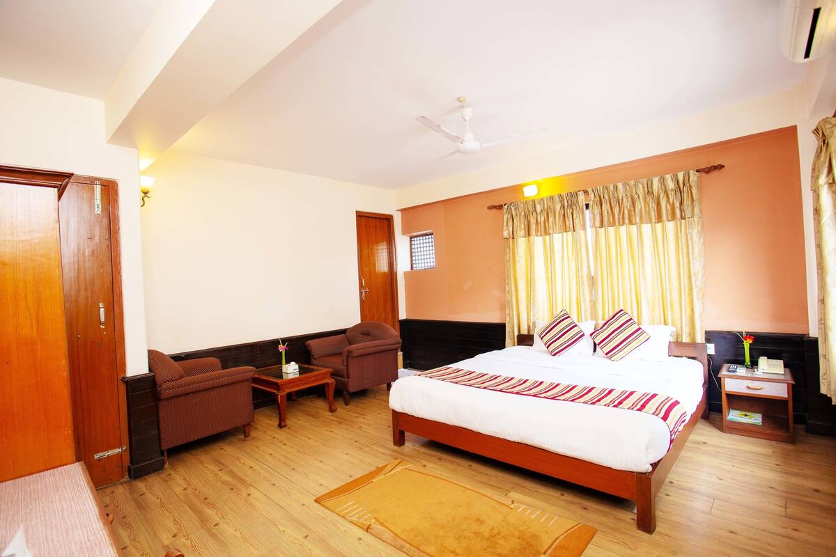 A hotel room with a large bed, a sofa, a small table, and a nightstand.