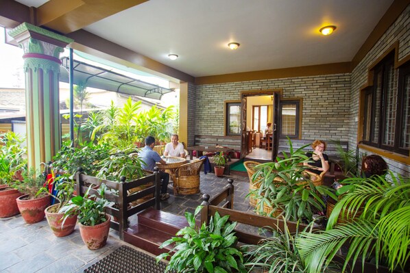 A spacious indoor area with multiple seating arrangements, potted plants, and a brick wall.