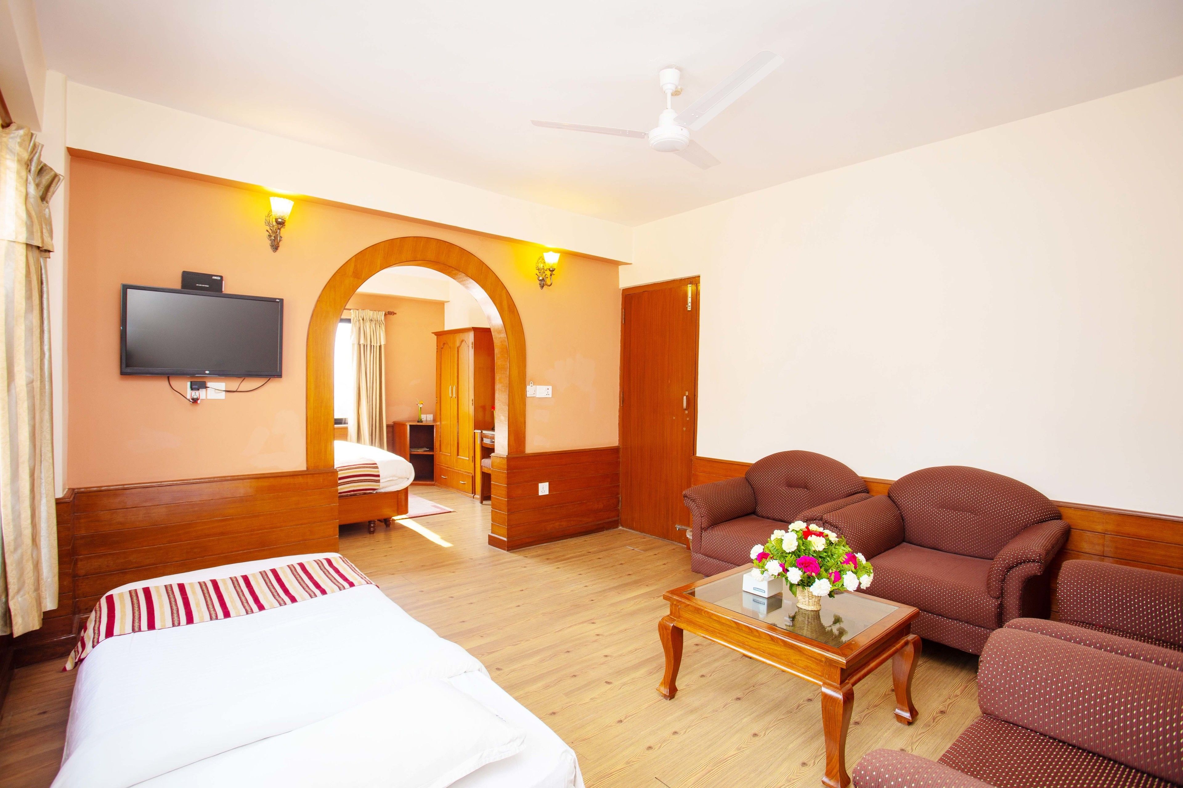 A hotel room with a bed, a sofa, a coffee table, a TV, and a ceiling fan.