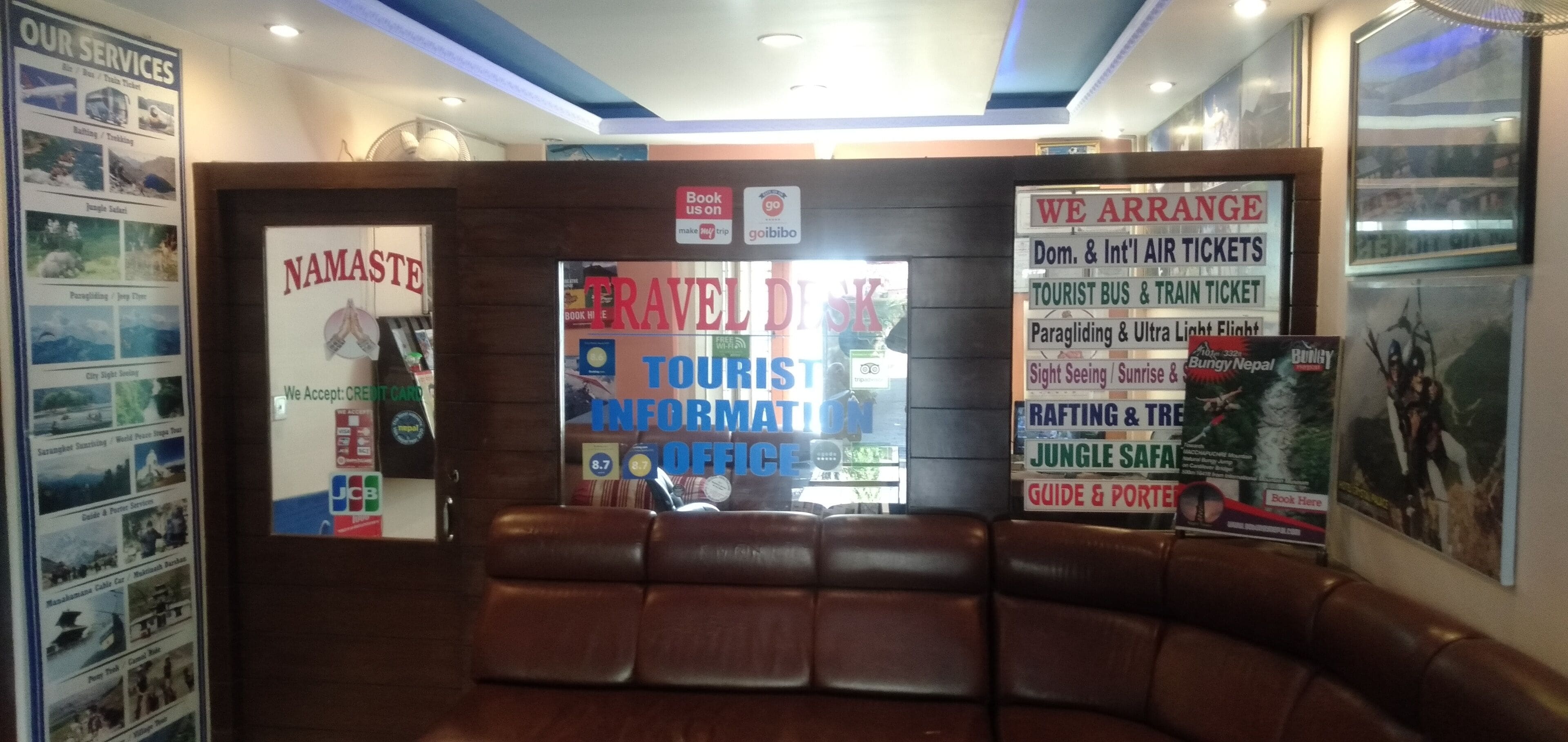 Un bureau d’information touristique avec un banc en cuir, une pancarte indiquant «Namasté» et divers affiches de voyage.