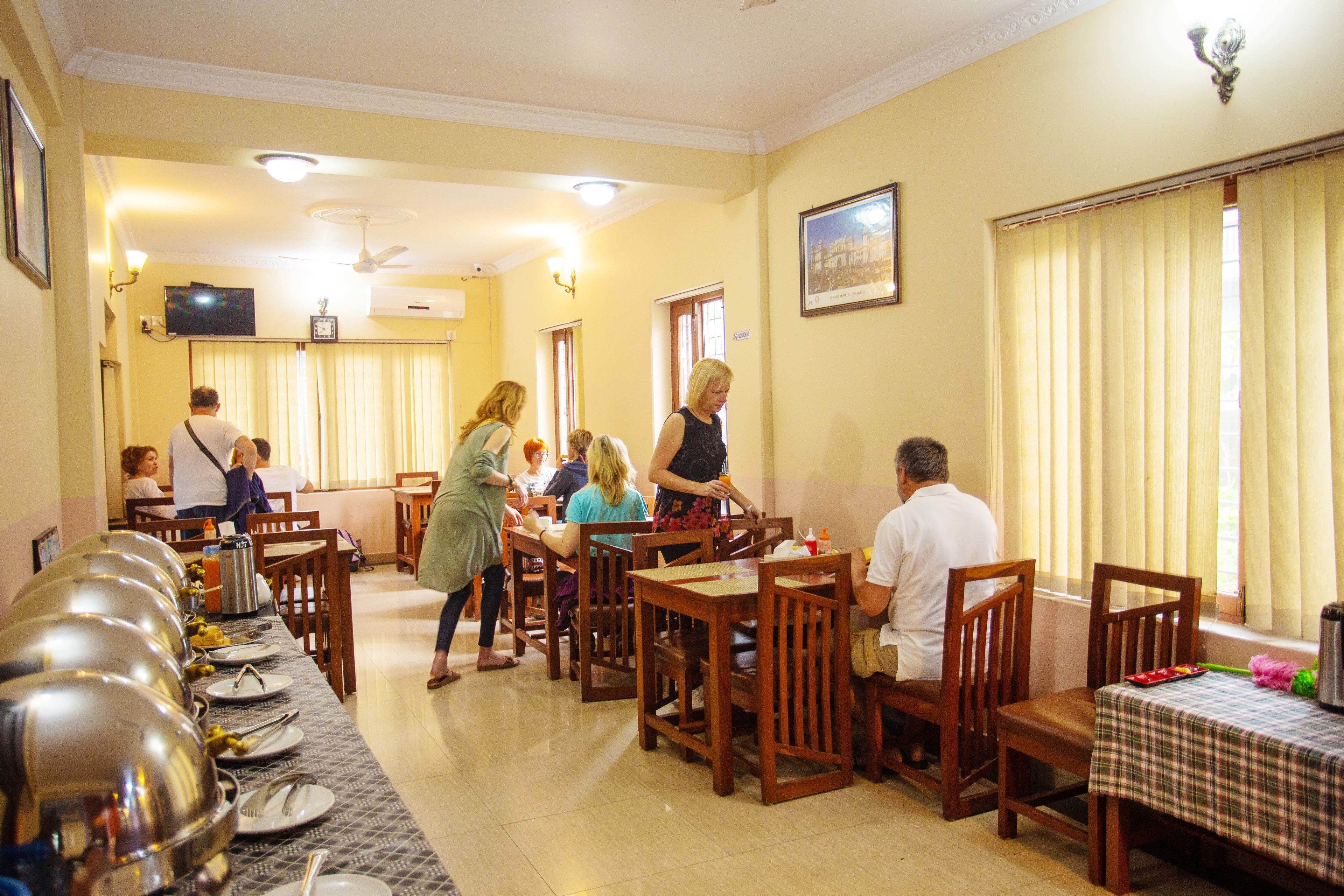 A dining area with multiple tables and chairs, a buffet line, and a television mounted on the wall.
