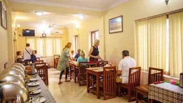Un espace repas comprenant plusieurs tables et chaises, un buffet et un téléviseur fixé au mur.