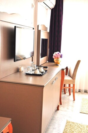 Ein Hotelzimmer mit Minibar, einem flachbildfernseher an der Wand, einem Holzstuhl und einer Vase mit Blumen auf der Ablagefläche.