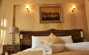 Ein Hotelzimmer mit einem hölzernen Kopfende, einem Bild an der Wand, zwei Wandleuchten, einer Nachttischlampe und einem ordentlich bezogenen Bett mit einem zusammengerollten Handtuch.