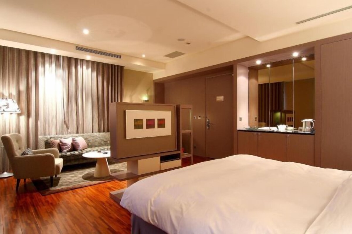 Habitación de hotel con cama, sofá, sillón, una mesita, televisor y armario.