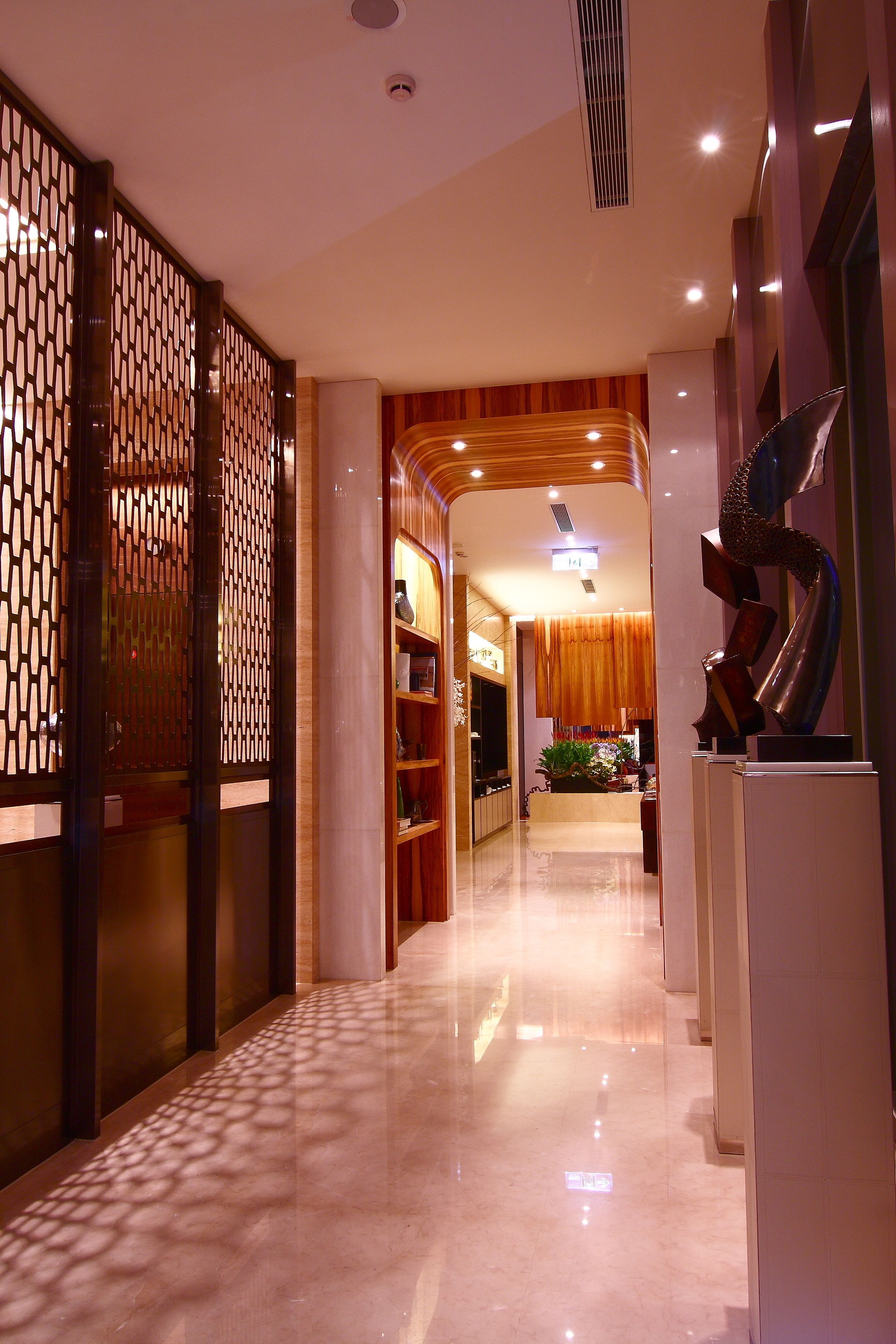 Un pasillo de hotel con un mostrador de recepción de madera, un revestimiento decorativo y una escultura moderna.