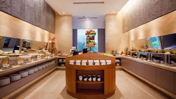A modern, well-lit hotel lobby with a central round table displaying various beverages, surrounded by counters with food and drink options.