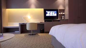 A hotel room with a bed, a desk with a lamp, a television, and a minibar.