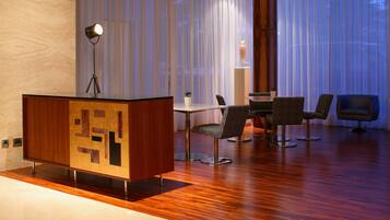 Een moderne hotelkamer met een houten vloer, een bureau met lamp en een zithoek met stoelen.