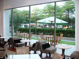 A cafe with outdoor seating, large windows, and a view of a busy street with cars and greenery.