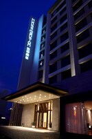 A modern hotel entrance with illuminated signage, a covered entryway, and a glass door leading inside.