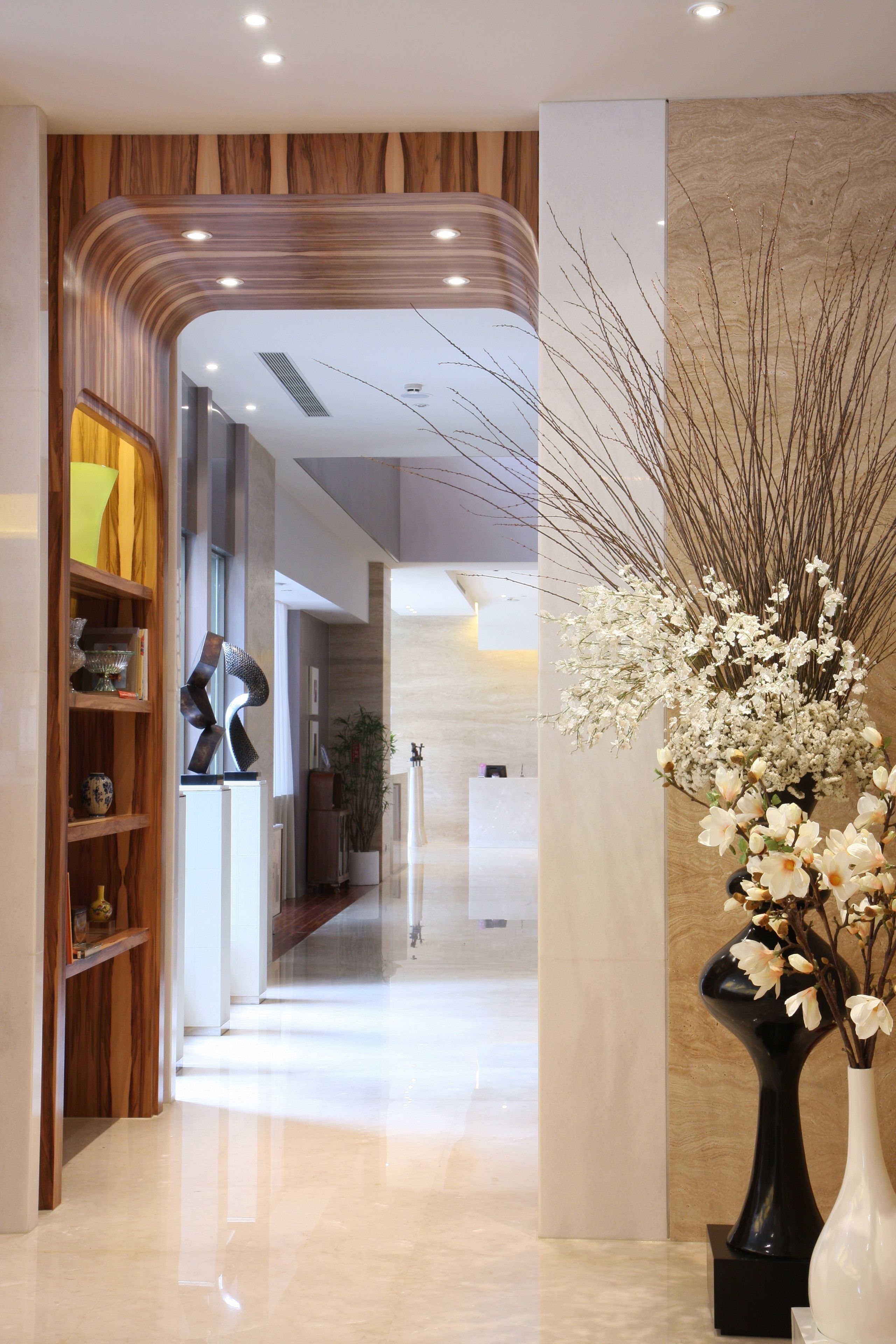 A modern lobby with a wooden reception desk, a black abstract sculpture, and a white vase with white flowers.