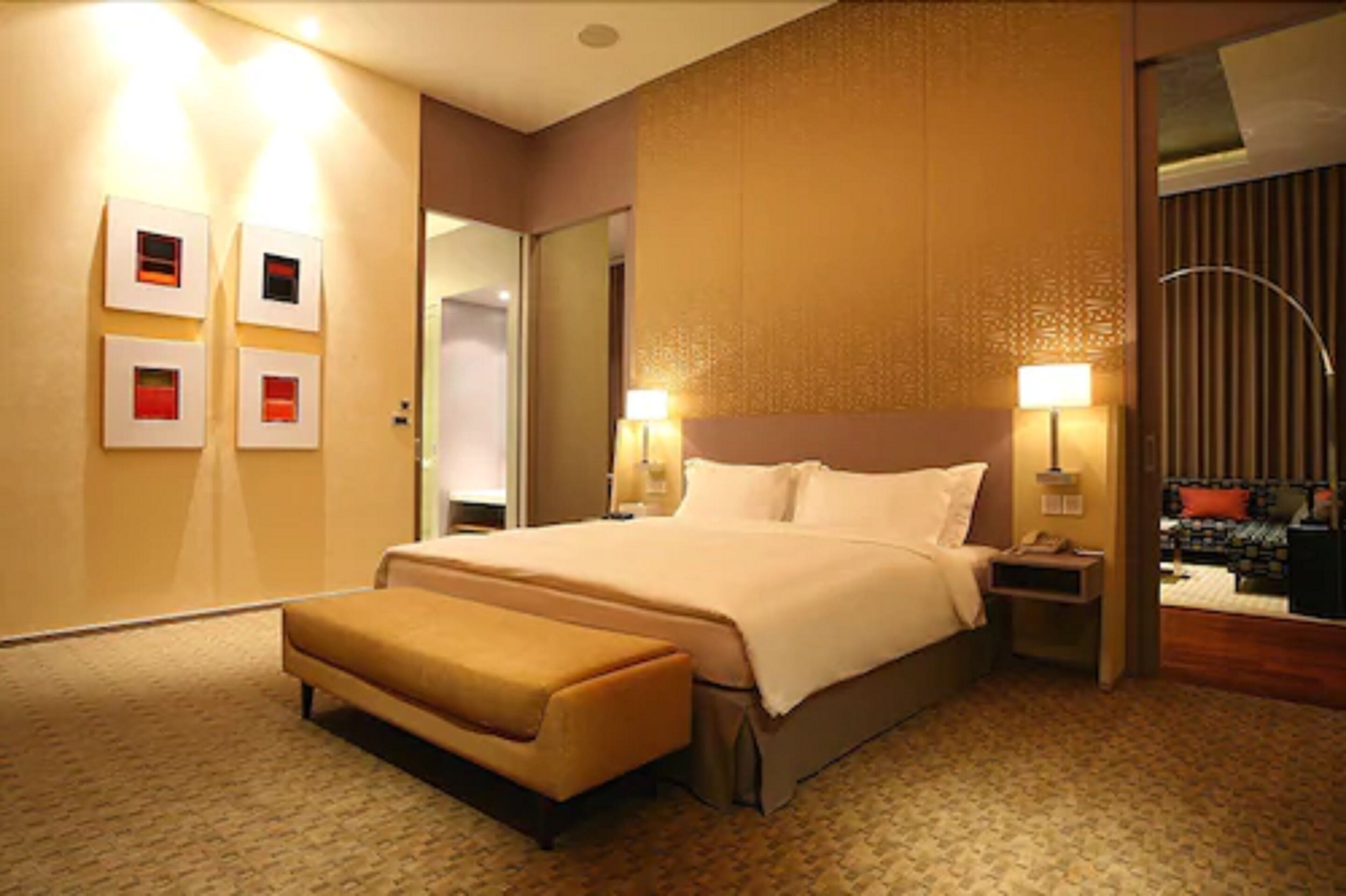 A hotel room with a large bed, a bench, two bedside tables with lamps, and a mirror on the wall.