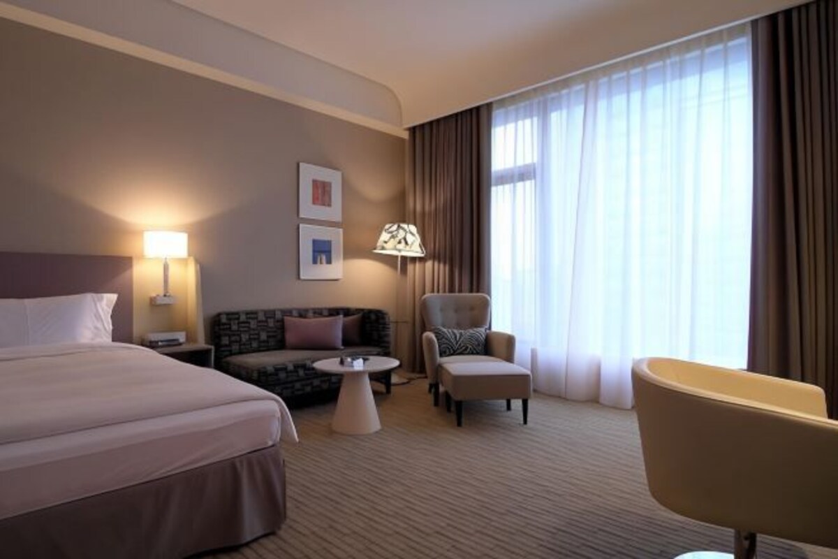 A hotel room with a bed, a sofa, a chair, a small table, and a window with curtains.