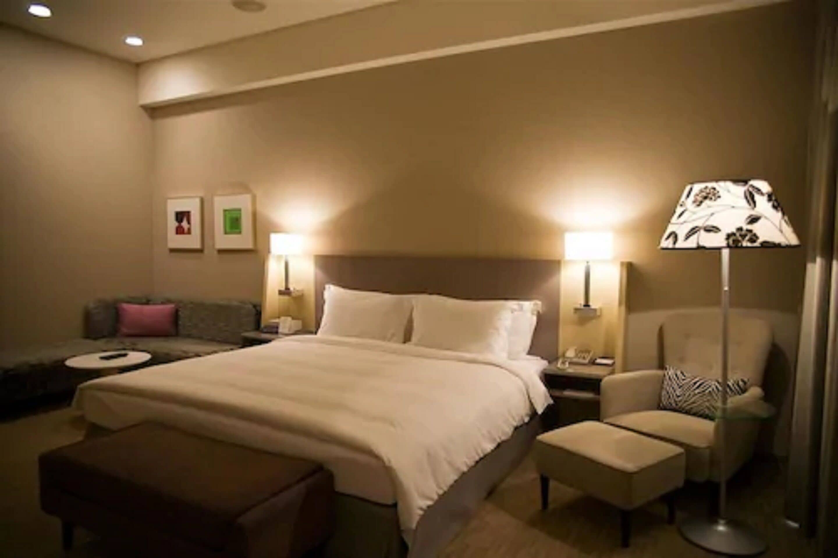 A hotel room with a large bed, a sofa, a chair, and a lamp.