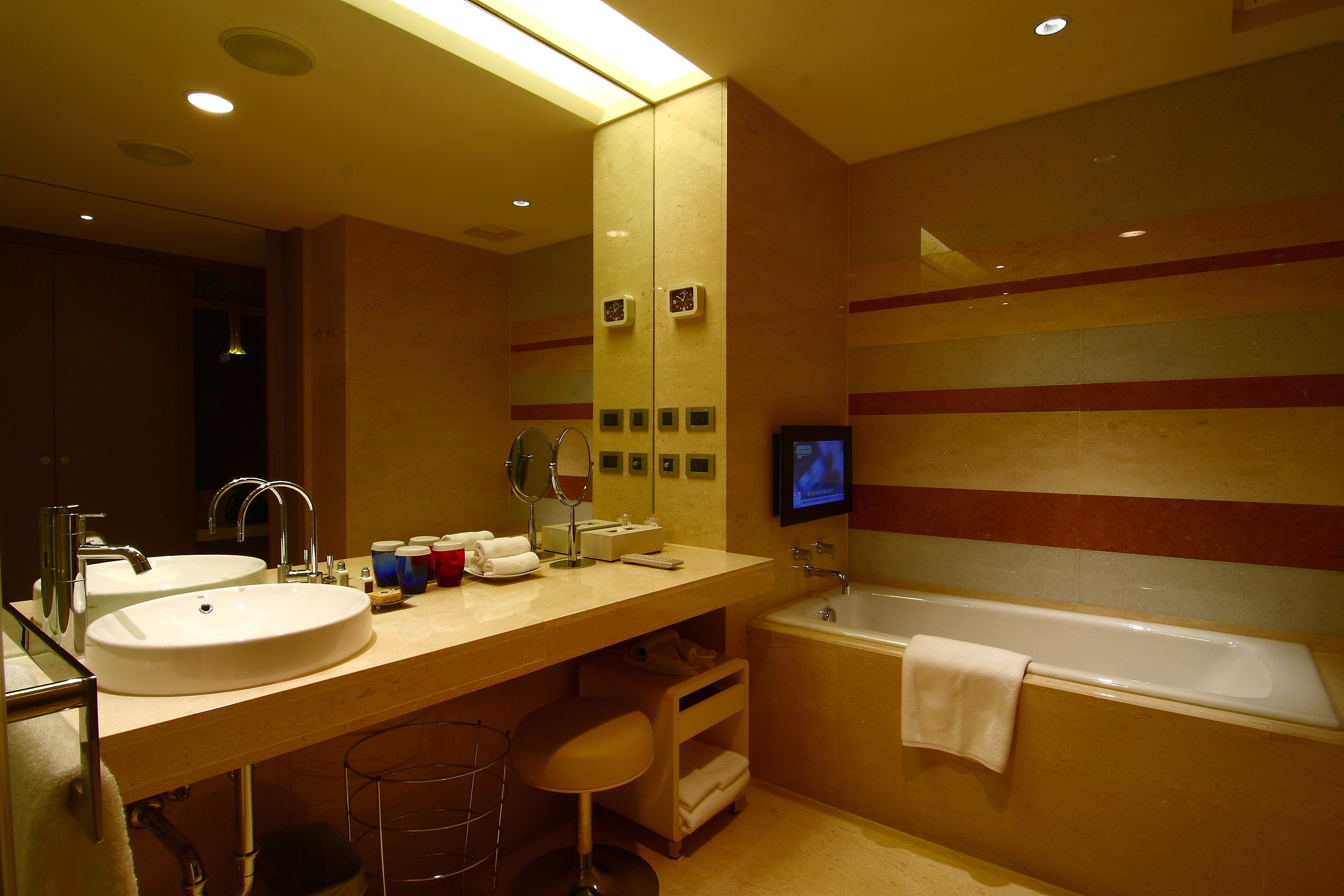 Un baño de hotel con dos lavamanos, una bañera, un espejo y un televisor.